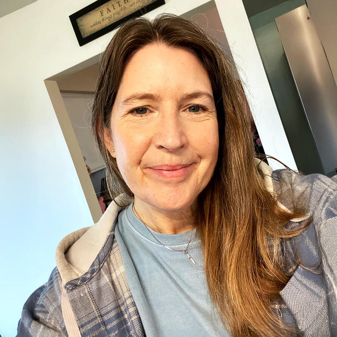 Dr. Kirsten Zellmer smiling indoors wearing a plaid jacket and blue shirt.